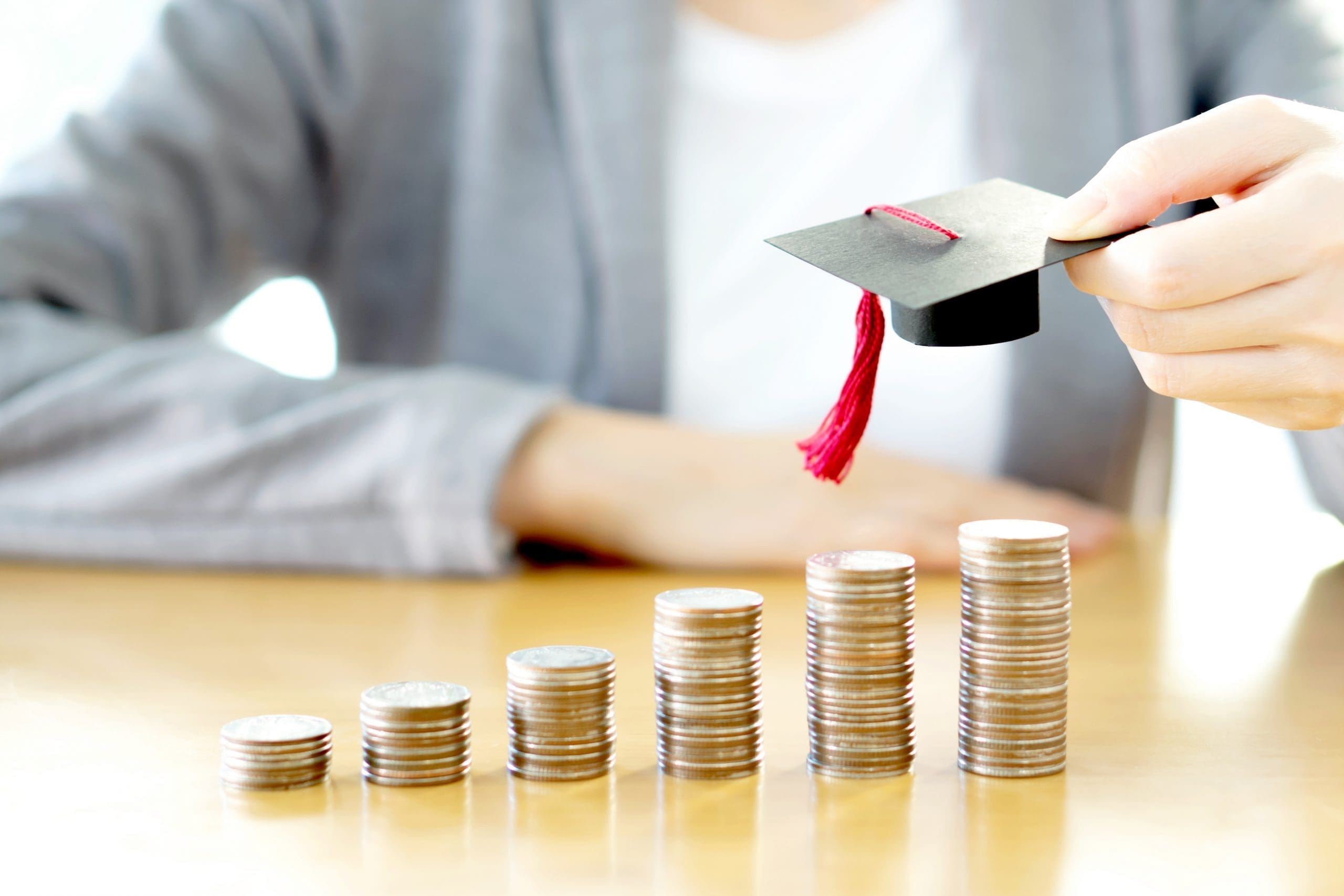 6 stacks of coins increasing in size with a small graduation cap.