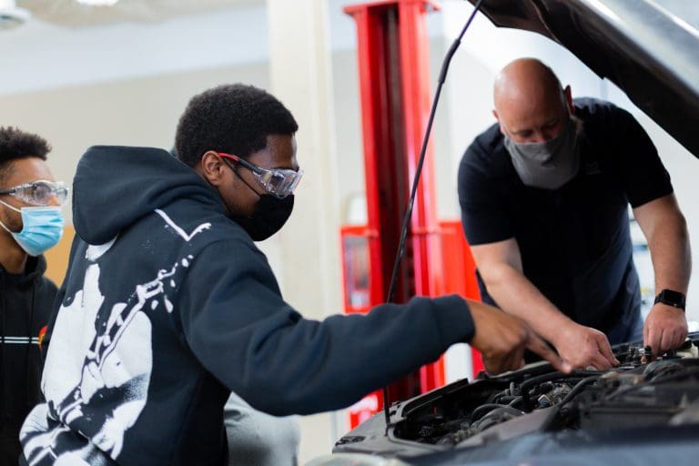 A student looks under the hood of a car, supervised by a Tidewater Tech instructor. Some of the cars students work on are Hyundai's which are made possible by those with Asian heritage in trades.