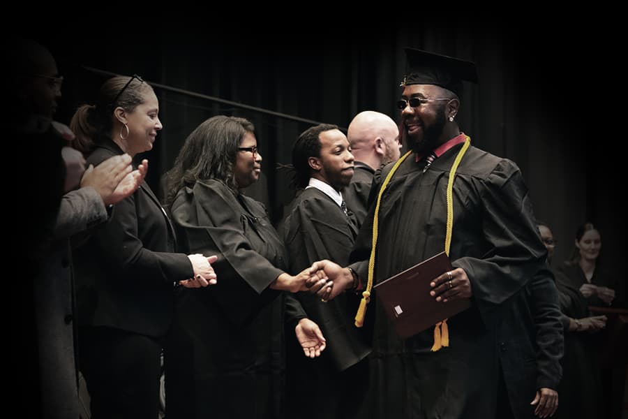A Tidewater Tech graduate walking across the stage, shaking hands with the staff and holding his diploma.