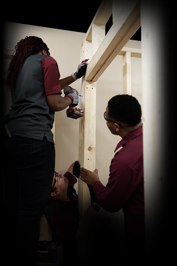 Tidewater Tech Building and Construction Trades students working with ladders and power drills, building a house frame in the lab.
