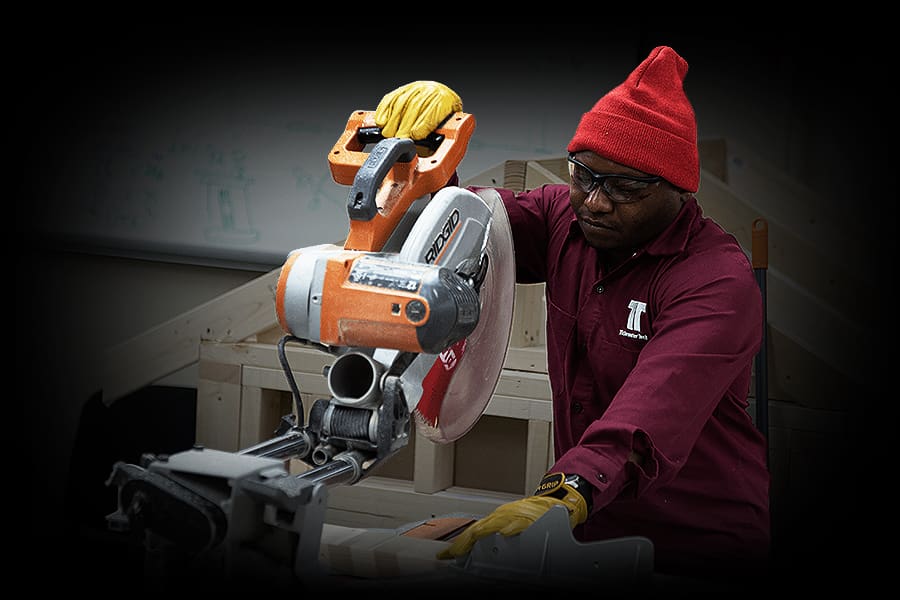 A Tidewater Tech building construction and trades student working with a miter saw in the lab.