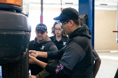 Automotive maintenance technician students working on a car.