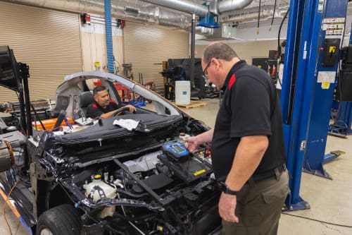 Automotive maintenance technicians using computers to run checks on a car.