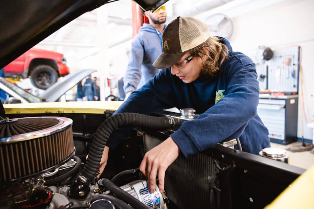 Student gains hands-on experience in a garage setting as part of auto technician programs, working under the hood to learn engine diagnostics and repair.