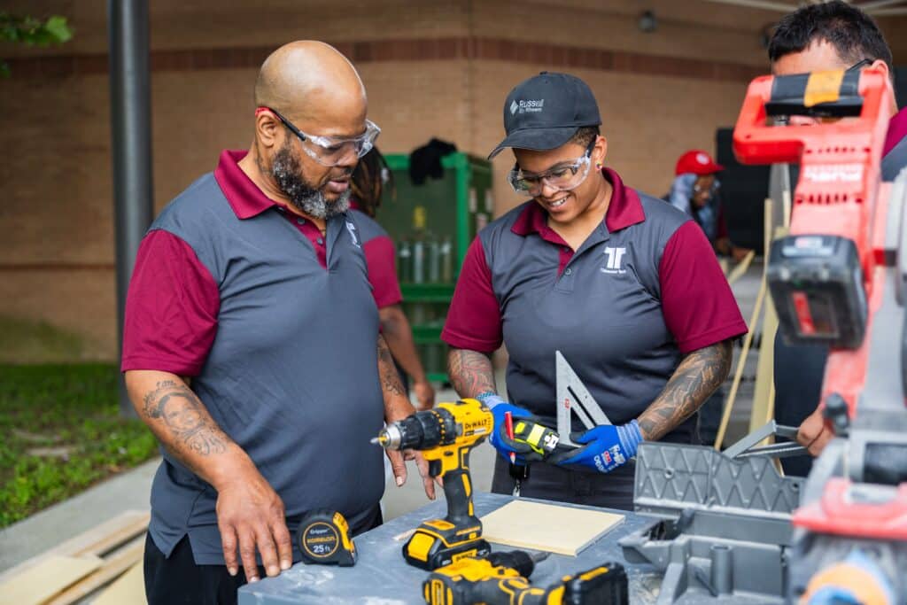 A woman in construction training uses power tools alongside a male peer, highlighting women in skilled trades.