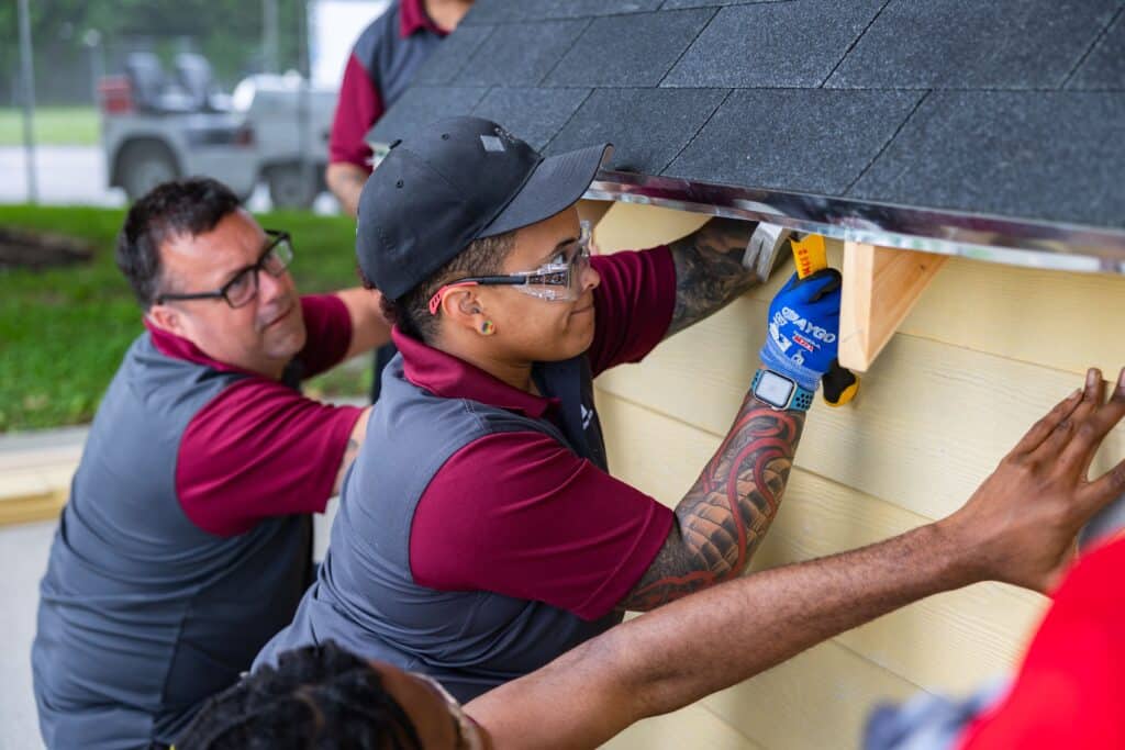 Woman in construction training uses a hammer while working on a structure alongside classmates.