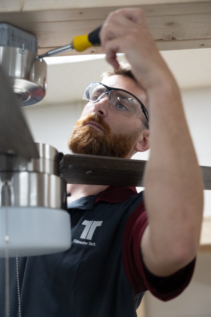 Tidewater Tech student installing a ceiling fan during an electrical component of the construction training program, demonstrating precision and technical skills.
