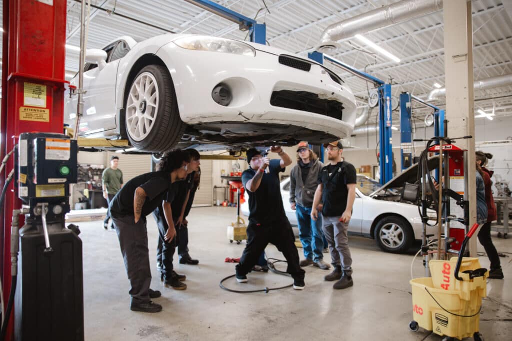 4 students looking underneath a car at a shop